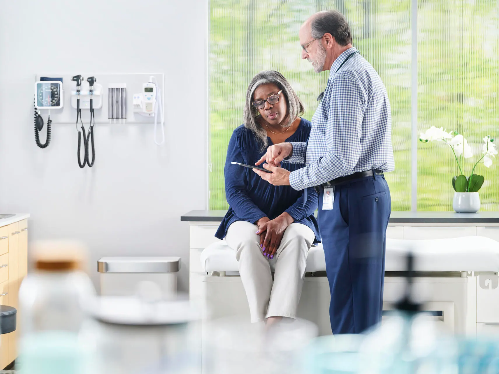 Physician in an examination room shows a patient something on his mobile phone